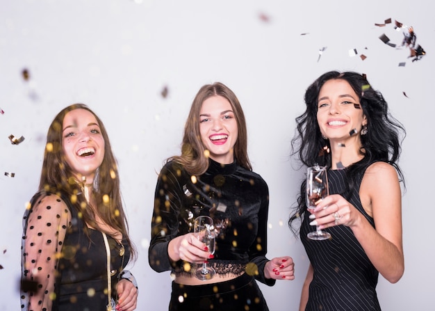 Happy women standing with champagne glasses under spangles 