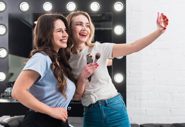 Счастливые женщины, принимающие селфи в зеркало для макияжа