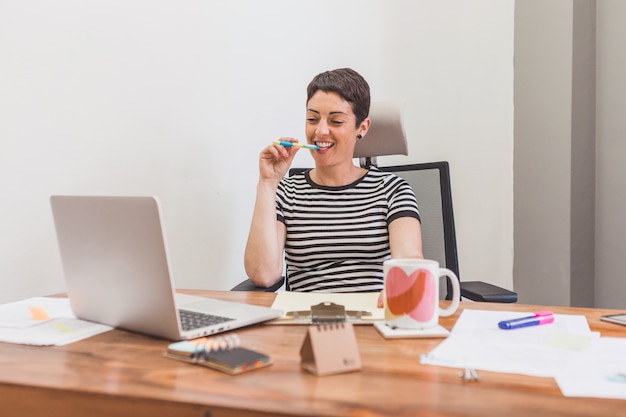 Happy worker with pen in her mouth looking at her laptop