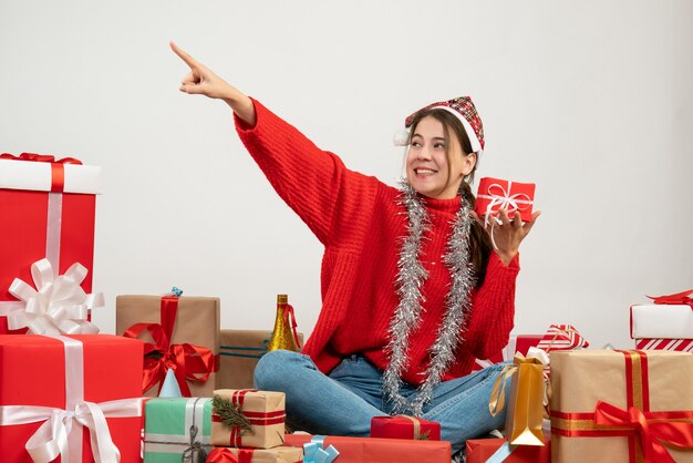 happy xmas girl with santa hat holding present sitting around presents on white