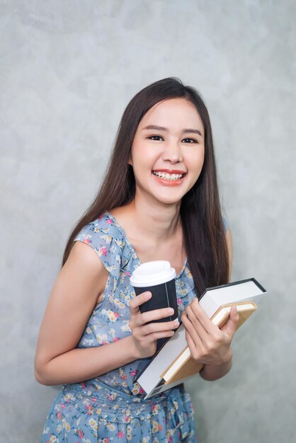 Happy young adult woman holding textbook and coffee cup in education concept