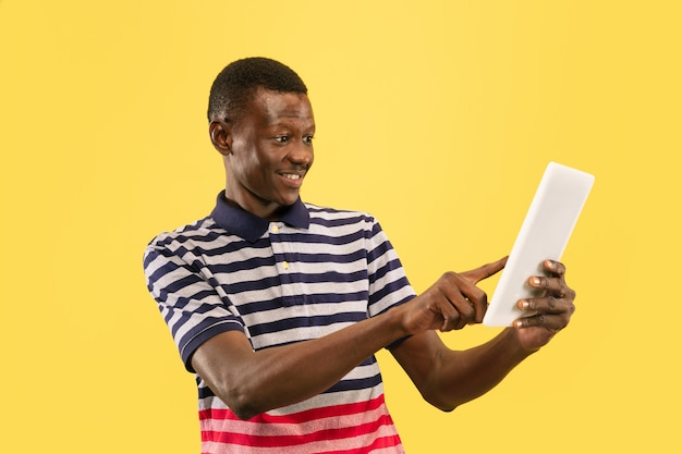 Happy young african-american man with tablet isolated on yellow studio