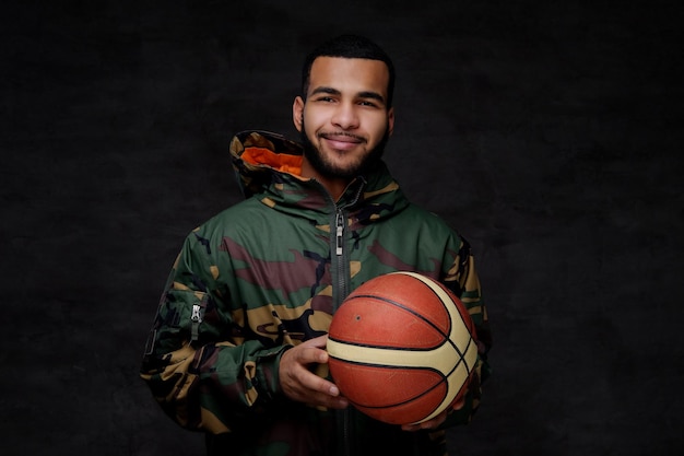 Free photo happy young african-american street basketball player in a camouflage jacket. isolated over dark background.