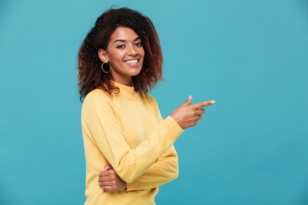 Happy young african lady dressed in warm sweater pointing.