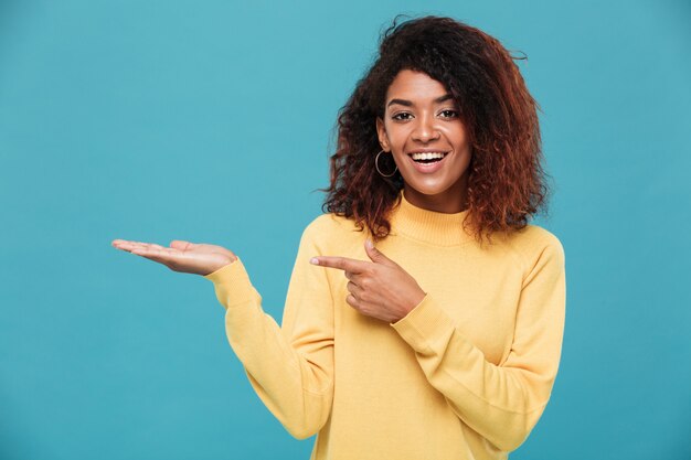 Happy young african lady dressed in warm sweater pointing.