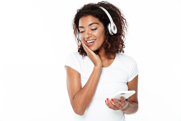 Happy young african lady listening music in headphones.