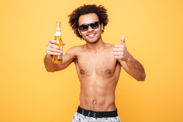 Happy young african man drinking beer showing thumbs up.