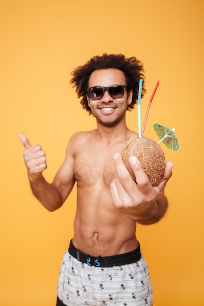 Happy young african man drinking cocktail and showing thumbs up.