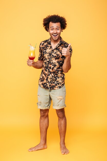 Happy young african man drinking cocktail and showing thumbs up.