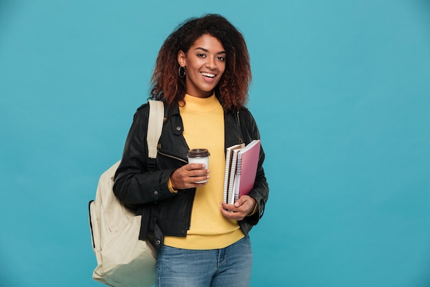 Happy young african woman holding notebooks and coffee.