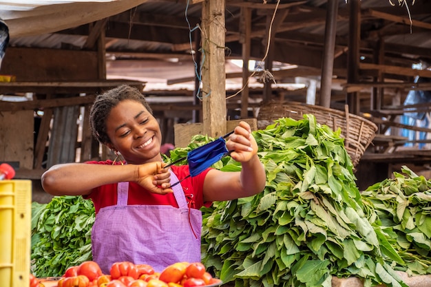 Happy young African woman in a local African market holding a face mask playfully