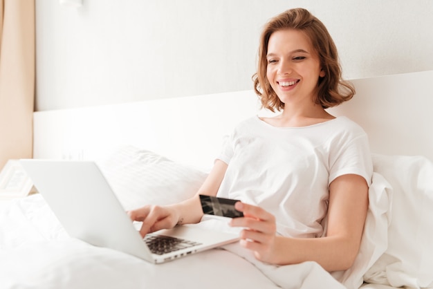 Happy young amazing woman sitting indoors using laptop