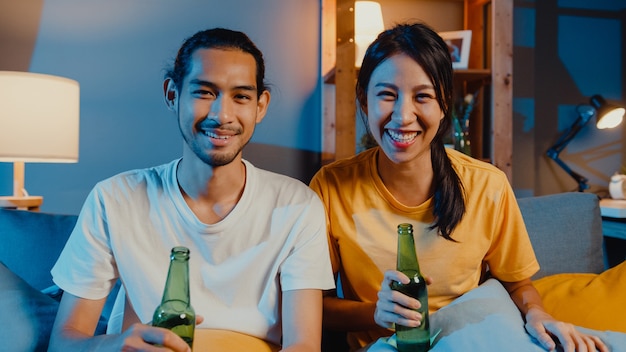 Happy young asian couple enjoy night party event sit couch in video call with friends