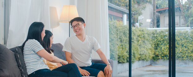 Happy young Asian family play together on couch at home. Chinese mother father and child daughter enjoying happy relax spending time together in modern living room in evening.