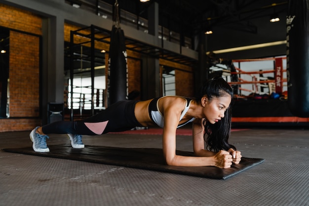 Happy young asian lady doing plank fat burning workout in fitness class.