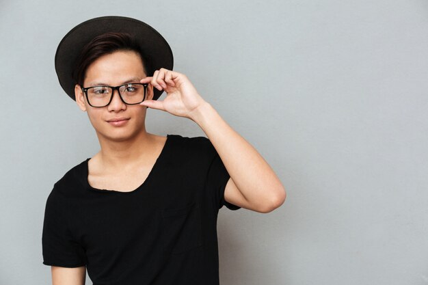 Happy young asian man standing isolated over grey wall