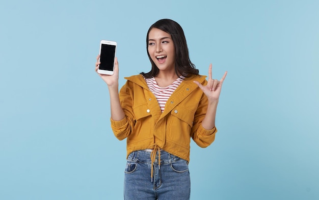 青い背景で隔離の空白の画面の携帯電話で示す幸せな若いアジアの女性