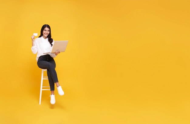 Happy young Asian woman showing credit card and using computer online shopping