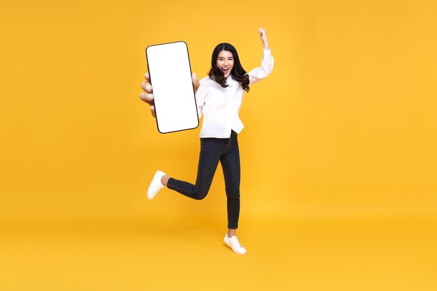 점프하는 동안 빈 휴대폰 화면을 보여주는 행복한 젊은 아시아 여성