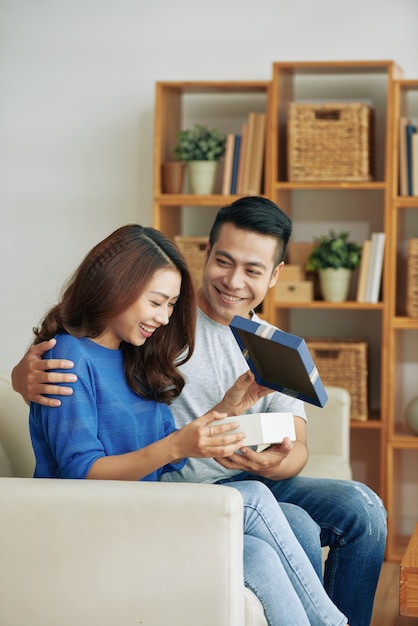 Happy young Asian woman sitting on couch at home and getting present from husband