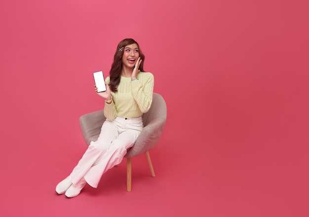 Happy young Asian woman sitting on sofa feeling happiness and gesture showing mobile smartphone