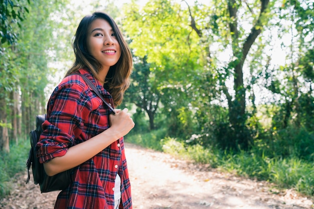 Happy young Asian woman traveler with backpack walking in forest.