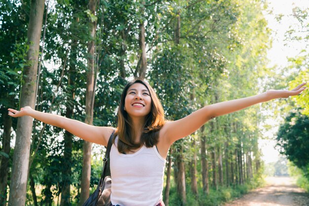 森を歩いてのバックパックと幸せな若いアジア女性旅行者。