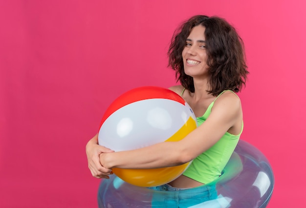 A happy young attractive woman with short hair in green crop top smiling and holding inflatable ball 