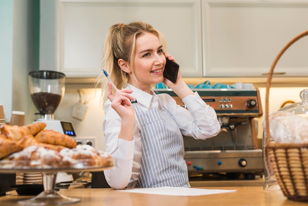 Foto gratuita felice giovane proprietario del negozio di panetteria prendendo l'ordine del telefono