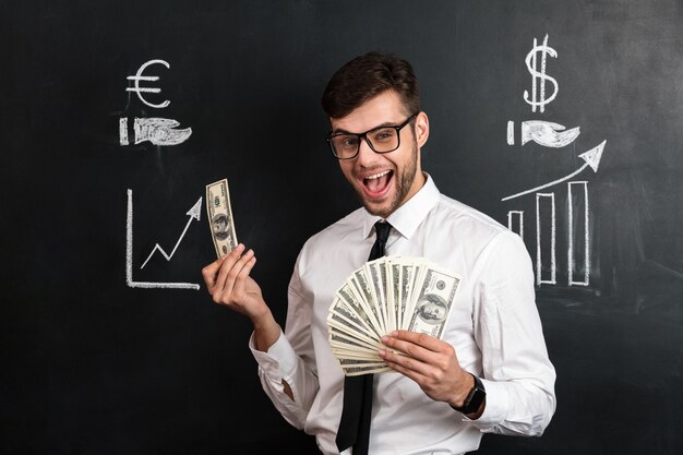 Happy young bearded man in glasses holding bunch of money