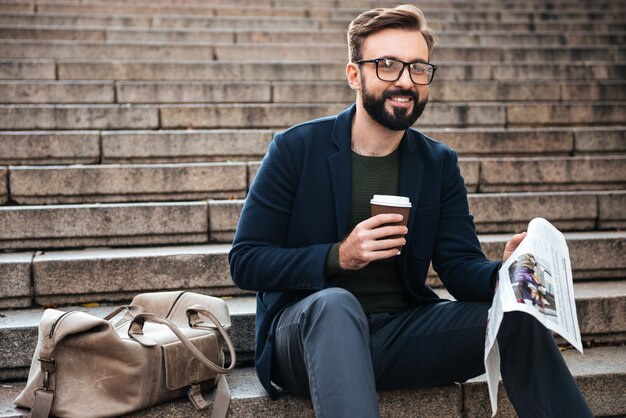 Happy young bearded man sitting outdoors on steps