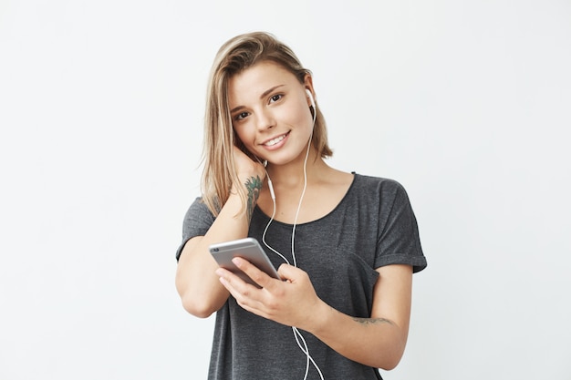 Happy young beautiful girl in headphones holding phone smiling .