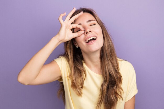 Happy young beautiful woman in beige t-shirt doing ok sign looking through this sign 