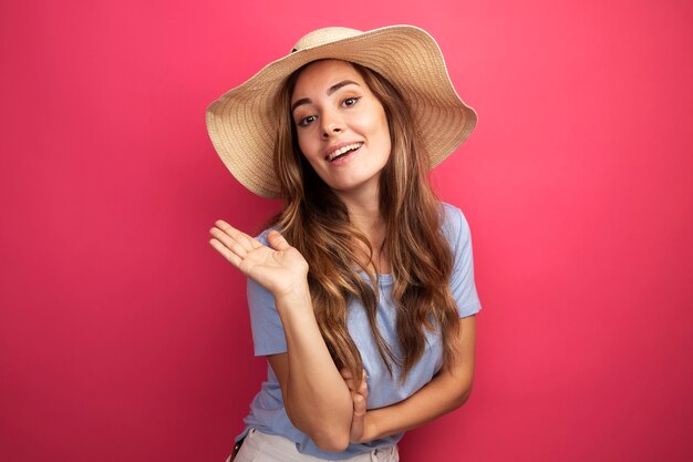 Happy young beautiful woman in blue t-shirt and summer hat looking at camera smiling waving