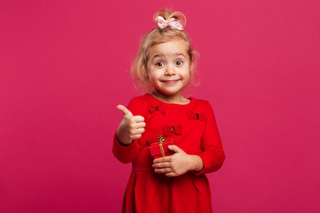 Счастливая молодая блондинка в красном платье, показывая большой палец вверх