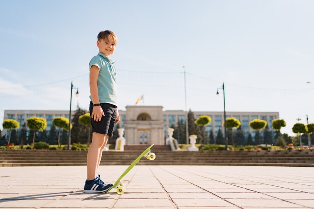 Happy young boy playing on skateboard in the park, Caucasian kid riding penny board, practicing skateboard.