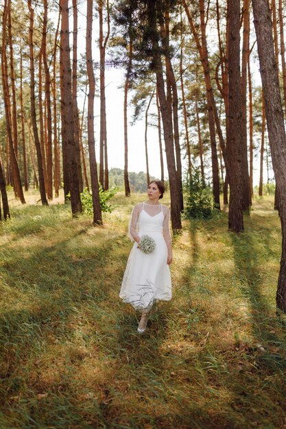 Happy young bride in a pine forest white wedding dress