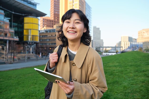Happy young brunette girl asian woman walks around city with tablet goes to university with her digi