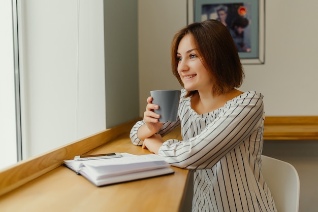 Happy young business woman sitting at table in cafe and thing about business and smiling