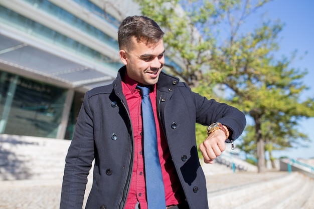 Free photo happy young businessman looking at watch outdoors