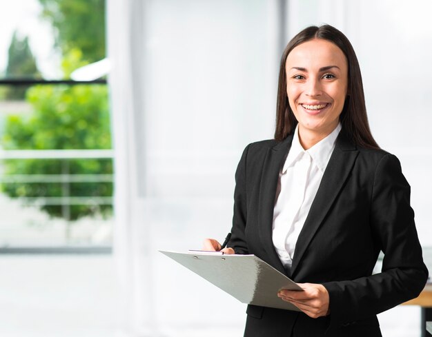 Happy young businesswoman holding clipboard and pen looking at camera