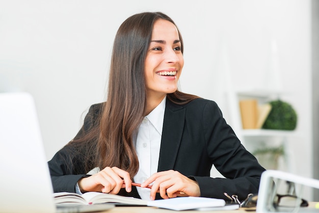 Happy young businesswoman sitting at office desk looking away