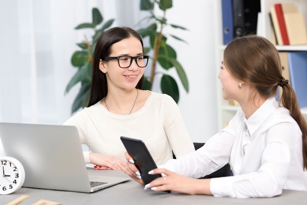 Happy young businesswoman sitting at workplace with digital tablet and laptop in the desk