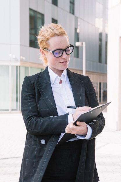 Happy young businesswoman writing on clipboard with pen