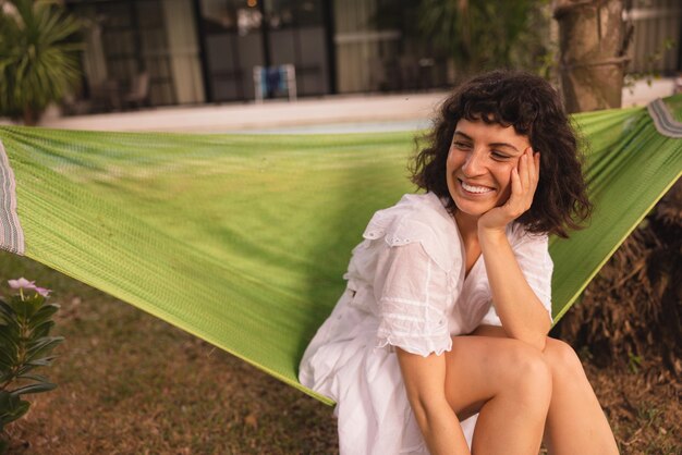 Happy young caucasian brunette woman smiling looks away sitting in hammock in backyard of country house Healthy lifestyle people concept