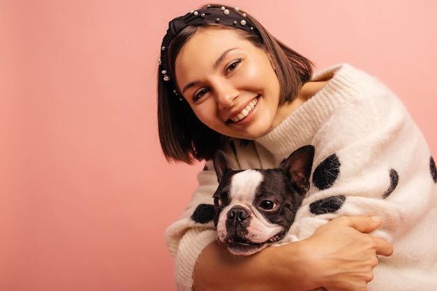 Happy young caucasian lady hugging french bulldog tightly while looking at camera on pink background Concept of protecting and helping animals