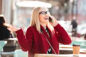 Free photo happy young caucasian lady talking by phone drinking coffee.