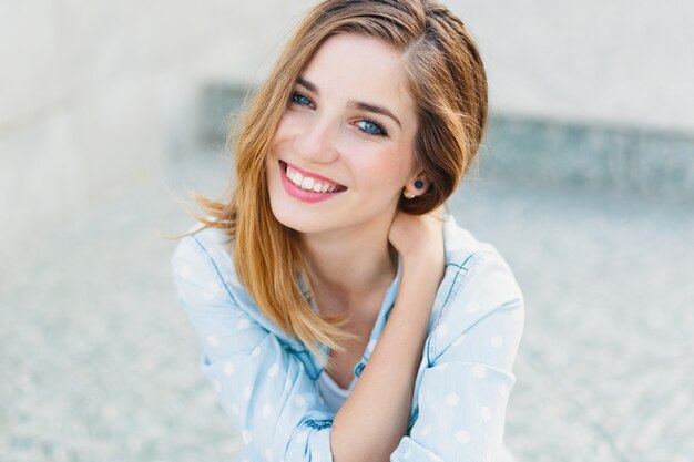 Happy young Caucasian woman demonstrating perfect teeth over light gray blurred background