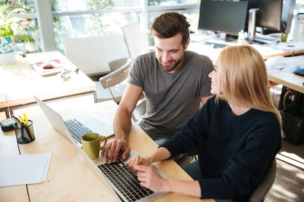 Free photo happy young colleagues sitting in office coworking using laptop