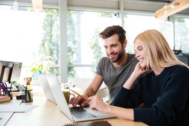 Happy young colleagues sitting in office coworking using laptop